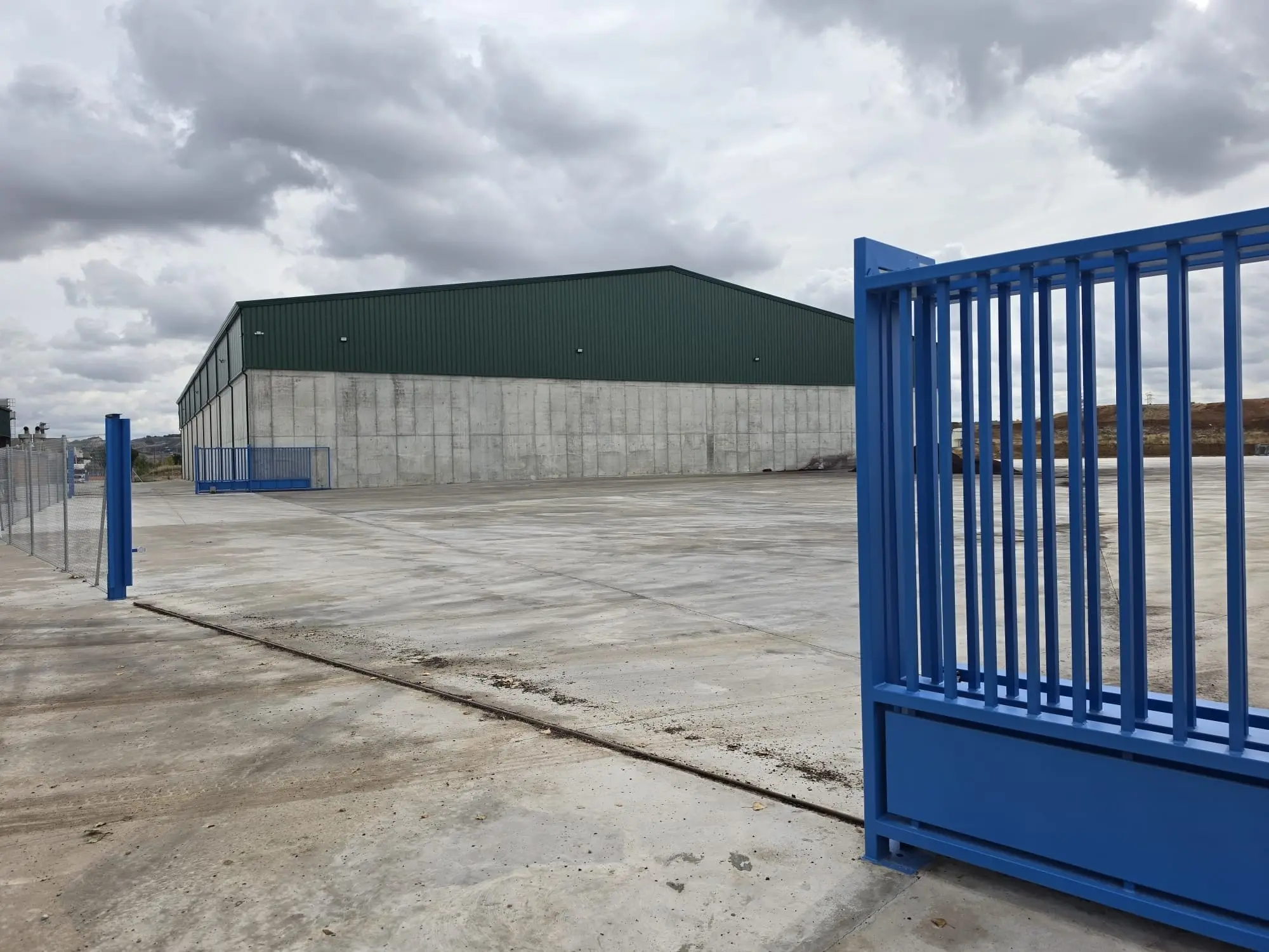 Puerta corredera azul de la parcela abierta frente a la nave