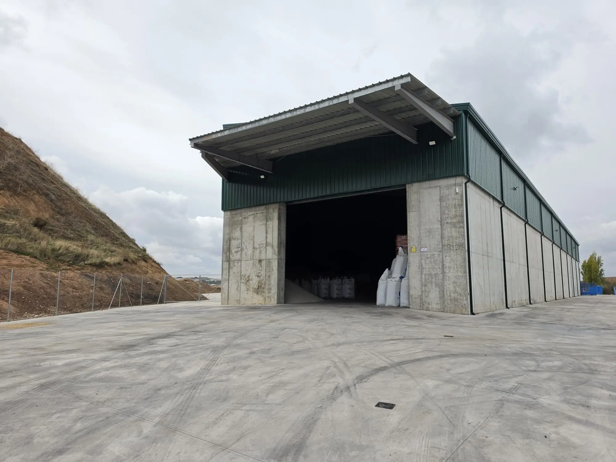 Nave de muros de hormigón con alero sobre la entrada, vista desde la explanada