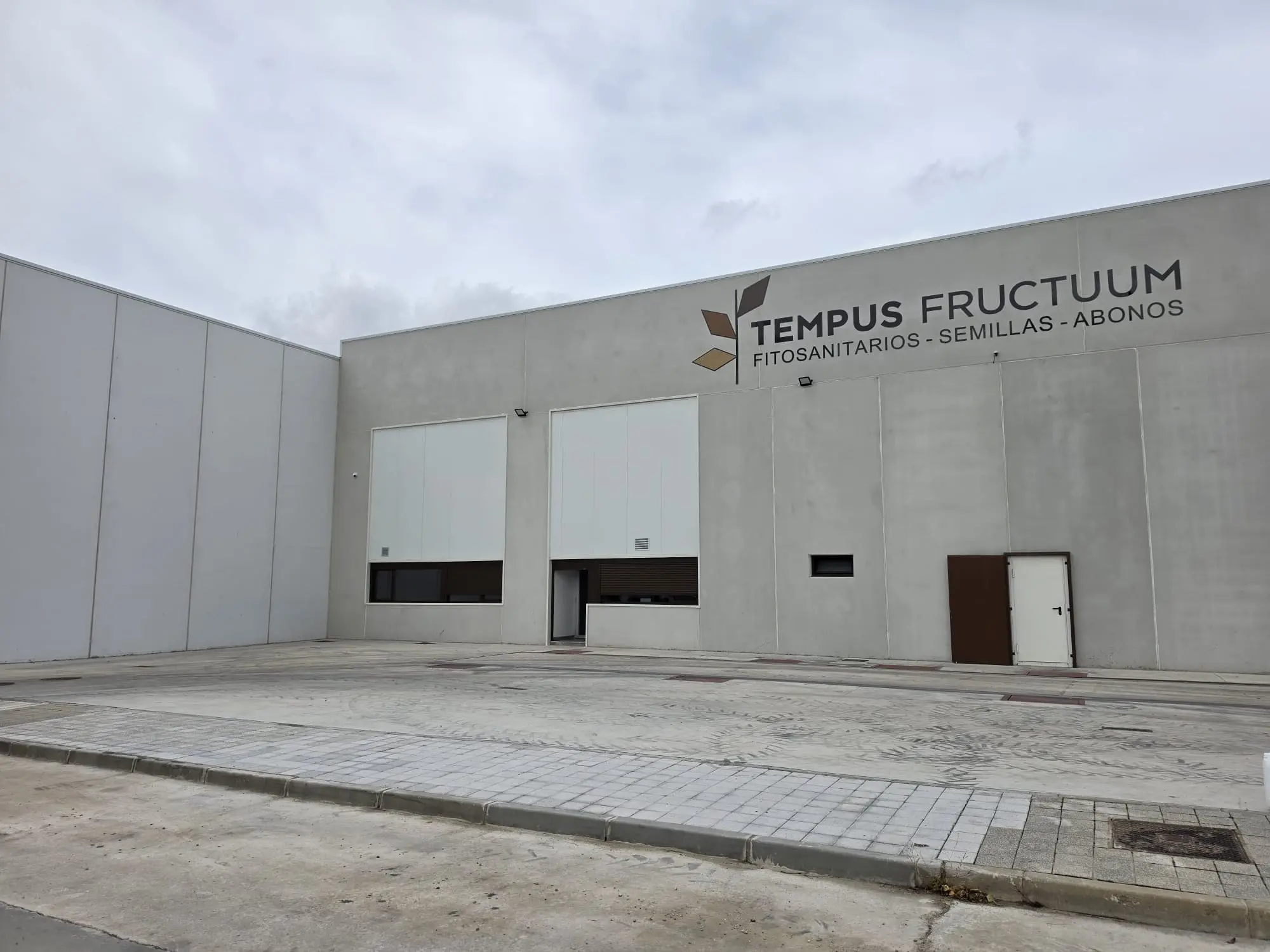 Fachada de la nave Tempus Fructuum con portones, puerta y el cartel de la empresa