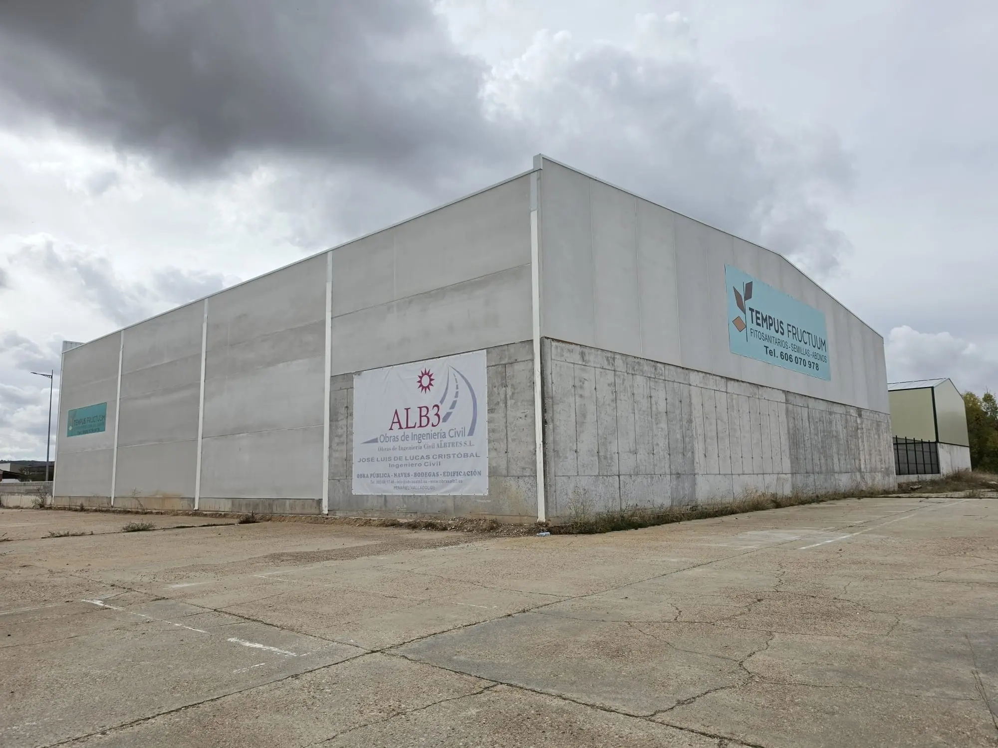 Lateral de la nave con zócalo de hormigón y el cartel de obra de ALB3