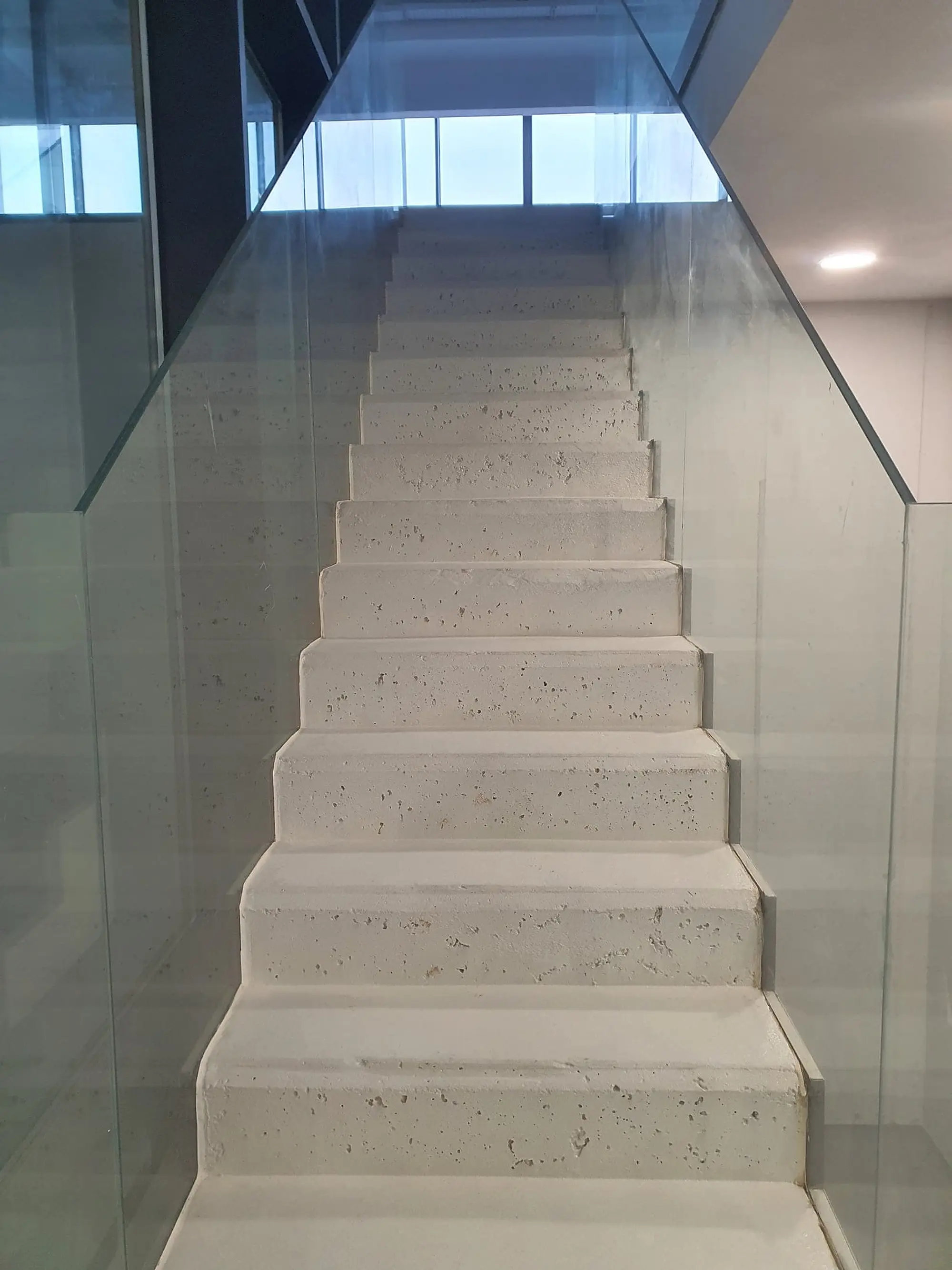 Escalera de hormigón entre paredes blancas, con barandilla de vidrio