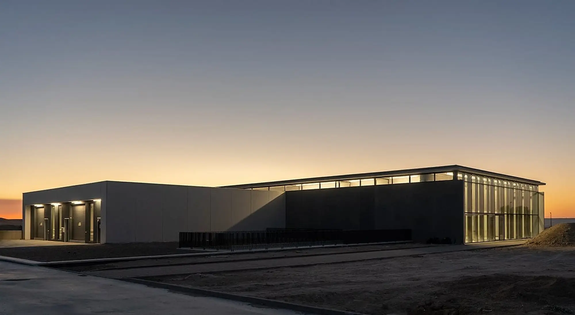 Fachada de la bodega al atardecer, con la nave iluminada por sus ventanales