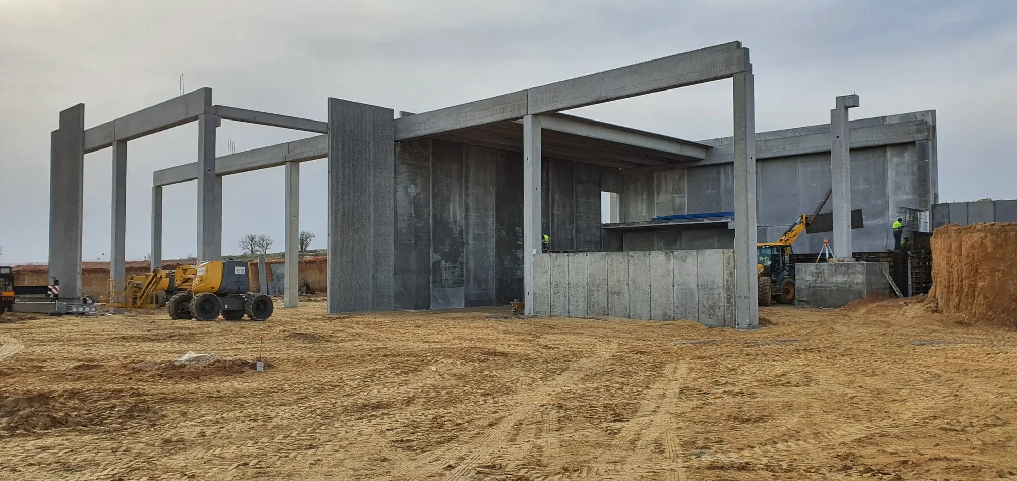 Estructura de pilares y vigas de hormigón de la bodega, con maquinaria sobre el terreno