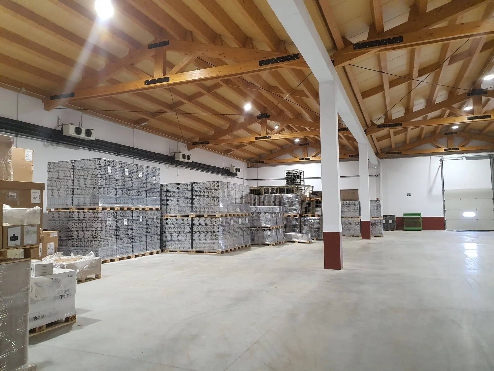 Nave de 2019-2020 con suelo de hormigón pulido, cerchas de madera y palés apilados