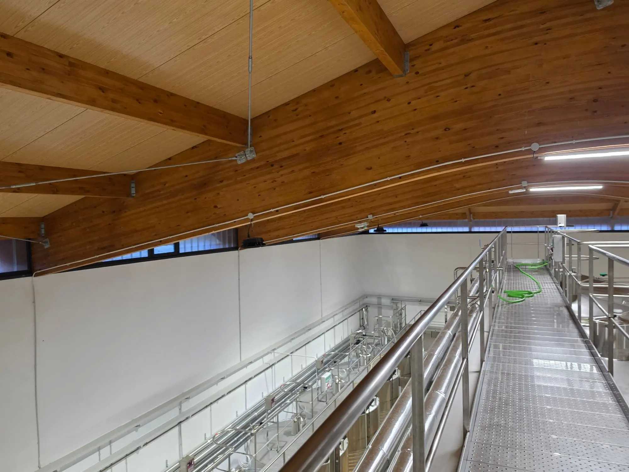 Pasarela de rejilla sobre los depósitos, junto a las vigas de madera y la franja de ventanas