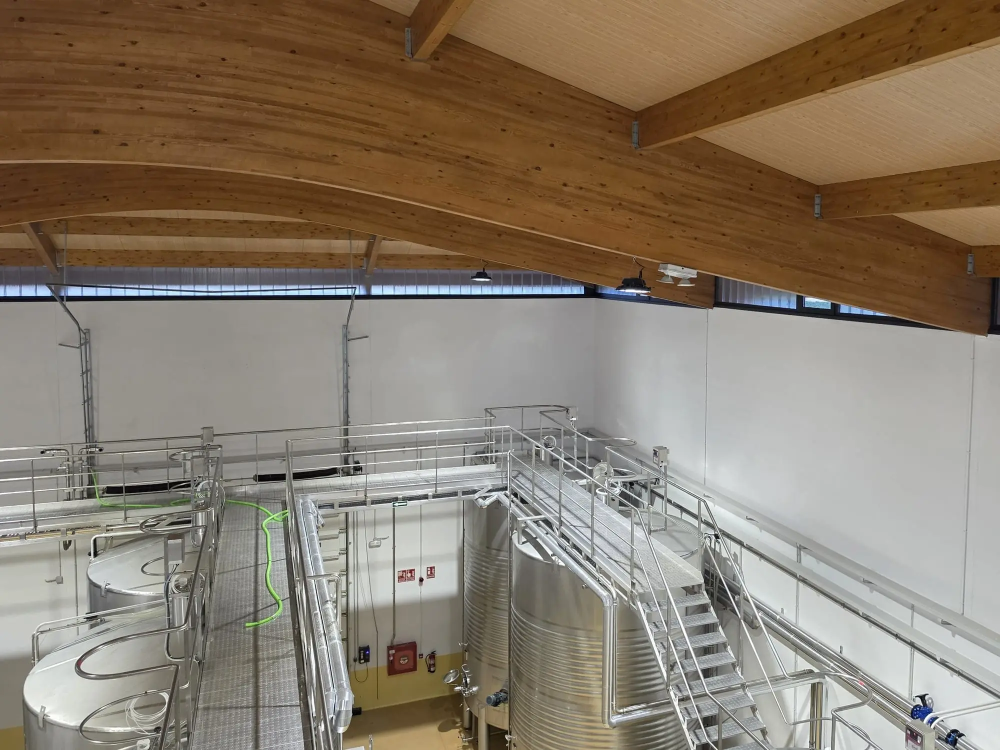Depósitos de acero inoxidable con pasarelas y escaleras bajo vigas de madera laminada en la ampliación de Protos en La Seca