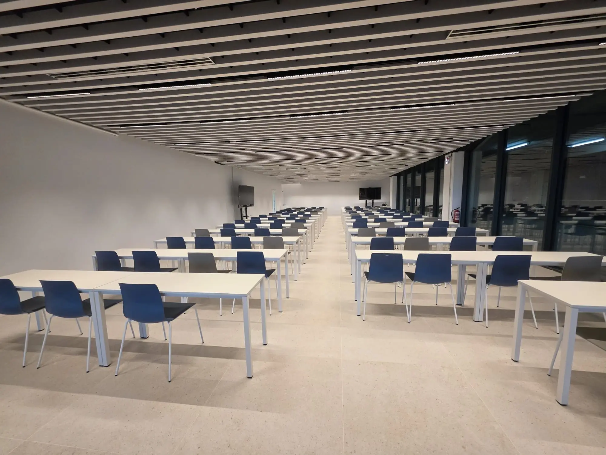 Gran sala con mesas en filas y ventanales a la derecha