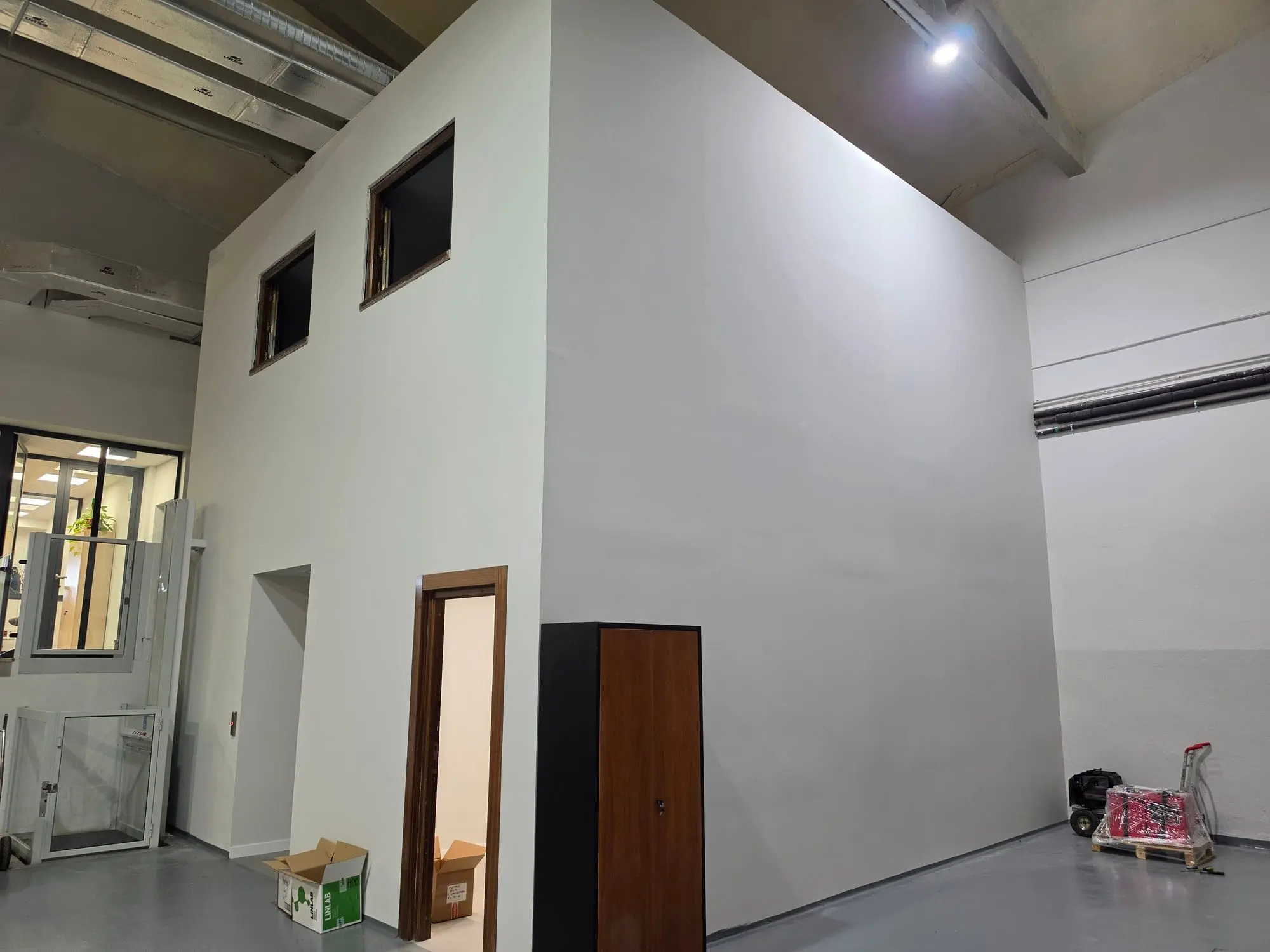 Volumen nuevo de oficinas en obra, con ventanas altas y una puerta de madera