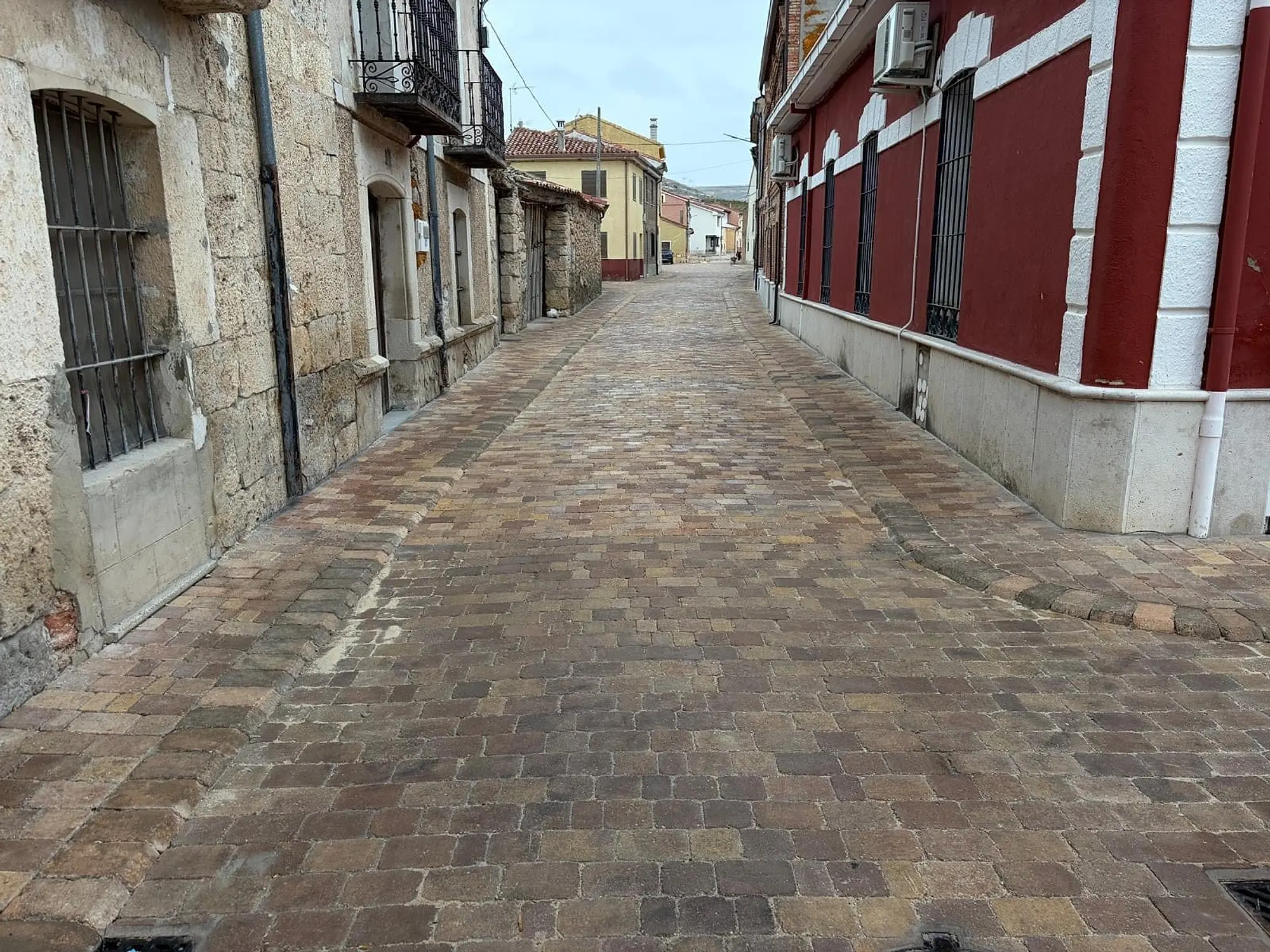 Calle estrecha adoquinada entre casas de piedra y una fachada roja