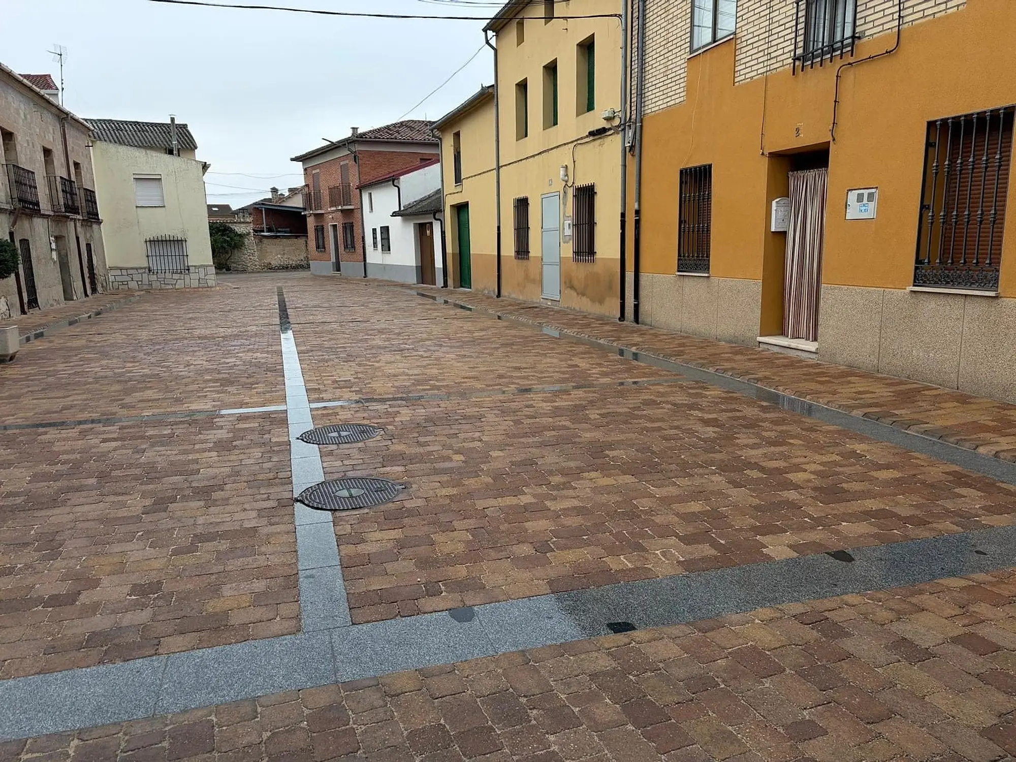 Calle adoquinada con una banda central de piedra gris y tapas de registro