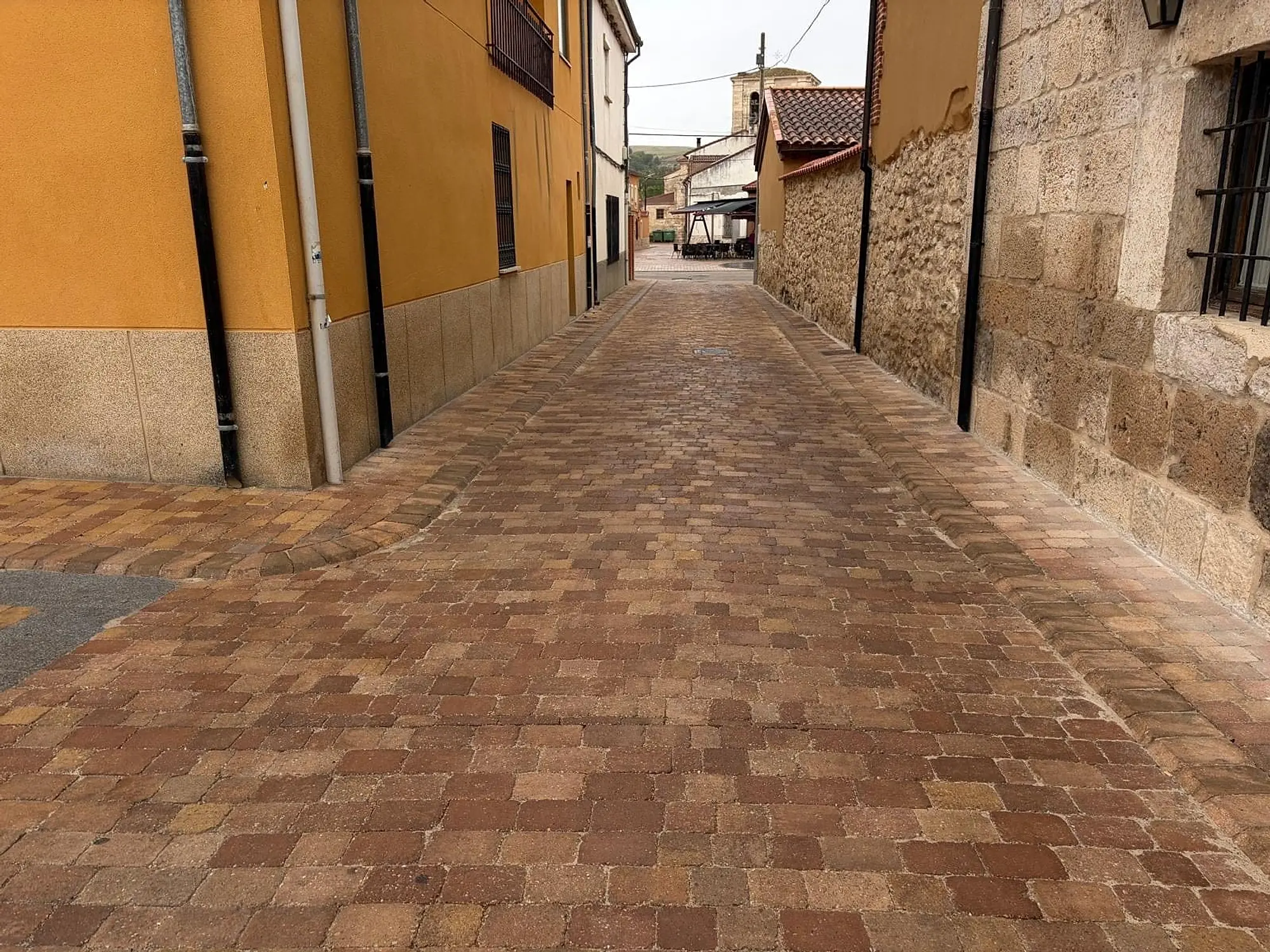 Calle adoquinada en cuesta entre fachadas amarillas y muros de piedra