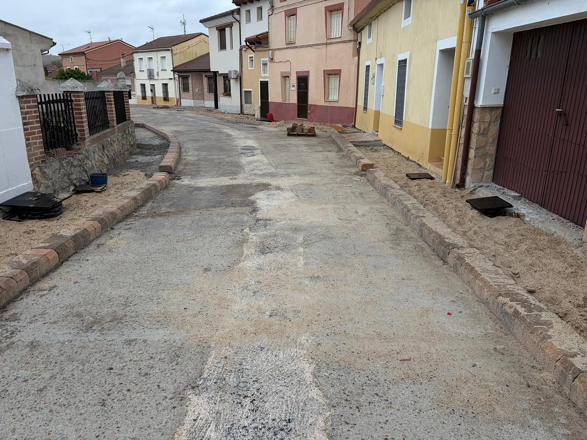 Calle en obra con los bordillos de las aceras ya colocados frente a casas de colores